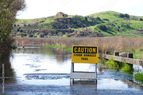 Caution, storm damaged trail sign up in front of flooded pedestrian trail along Coyote Canyon, northern california
