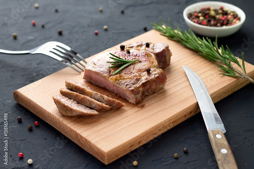 Φωτογραφία Tasty homemade well-done steak on wooden cutting board with fork and knife on stone background