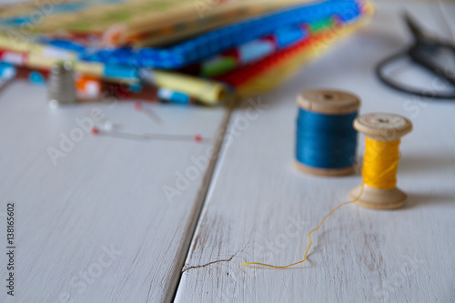 Colorful fabrics with vintage scissors, pins, measuring tape and rolling cotton threads on white wooden table photo