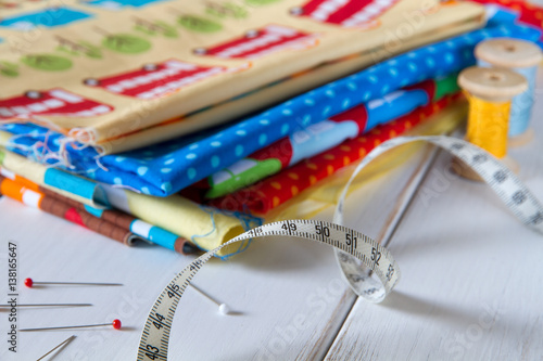 Colorful fabrics with pins, measuring tape and rolling cotton threads on white wooden table photo