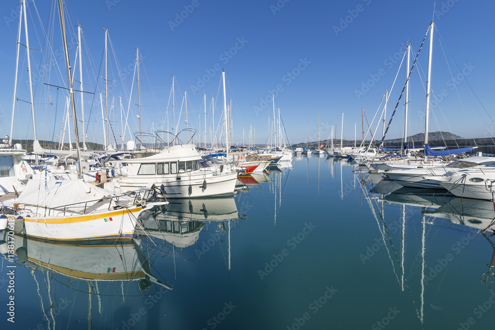 Wonderful mirror reflections of boats moored in the waters of the tourist port of Talamone, Grosseto, Tuscany, Italy