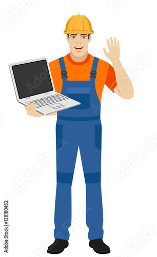 Builder with laptop greeting someone with his hand raised up
