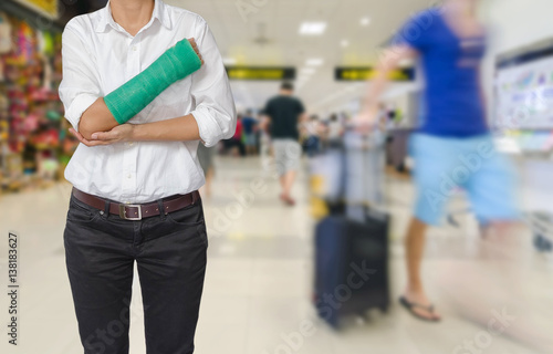 Injured woman with green cast on hand and arm on traveler in motion blur in airport interior background, ,body injury concept.