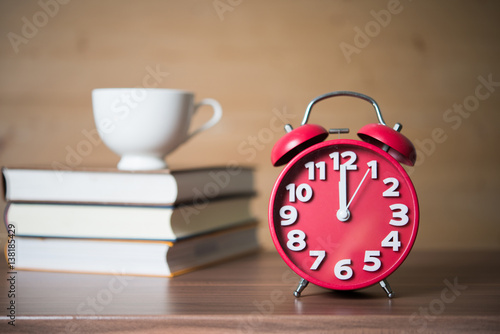 Concept of Education - Coffee cup on Pile of books with red alarm clock against wooden background.