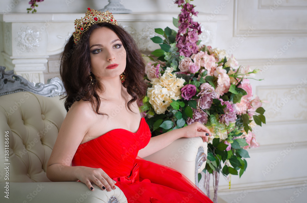 Beautiful woman in red long dress with a gold crown and earrings posing ...