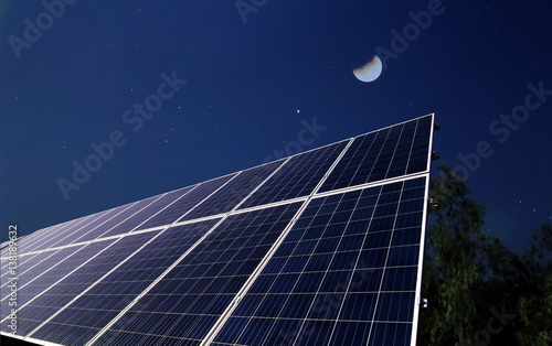Solar panels at night with the half moon before the sun rising