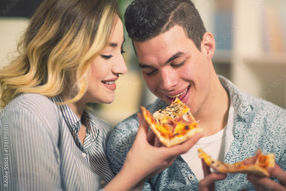 Couple relaxing at home and eating pizza.They are laughing and eating pizza and having a great time.