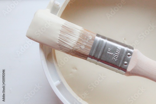 Used paintbrush resting on the edge of a cream paint pot