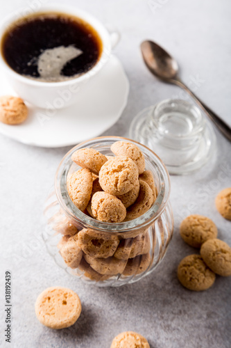 Amaretti cookies in glass pot with white cup of coffee on light gray background with copy space. High angle view