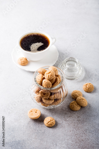 Amaretti cookies in glass pot with white cup of coffee on light gray background with copy space. High angle view