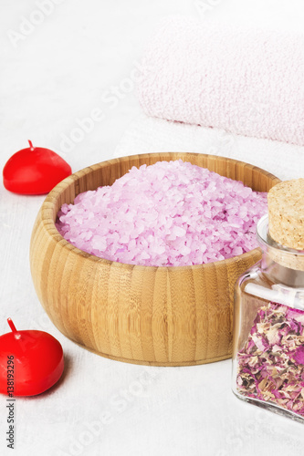 Bath salt with aroma of a rose in a wooden bowl, petals and a fresh pink rose, towels and candles on a white background