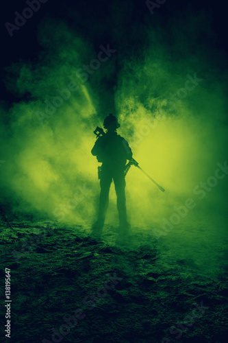 Army sniper with large caliber rifle standing in the fire and smoke. Backlit silhouette, toned image