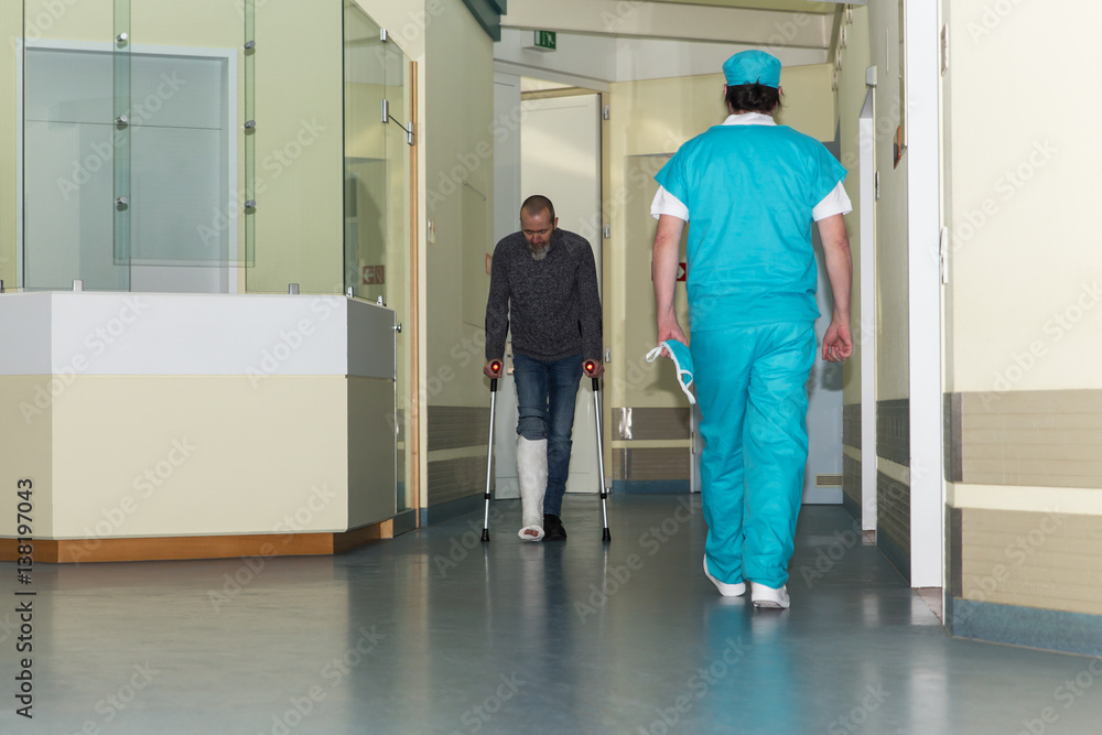 Station im Krankenhaus, Mann mit Beinbruch und Chirurg im Flur