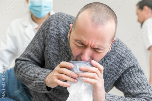 Foto Mann beim Erbrechen in Tüte, Ärzte im Hintergrund, Norovirus oder Infektion