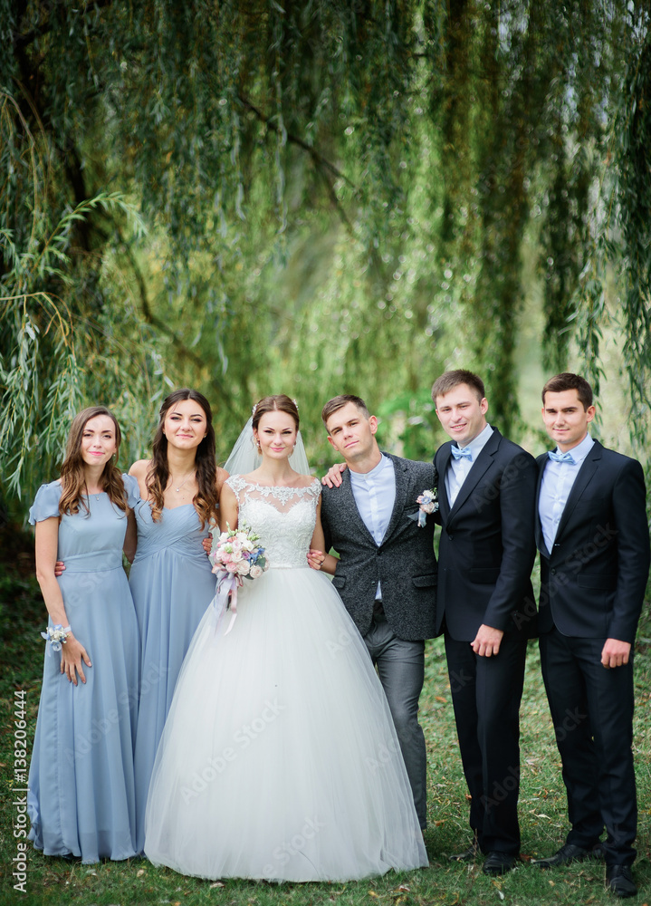 Newlyweds, groomsmen and bridesmaids in blue dresses pose under arch of greenery