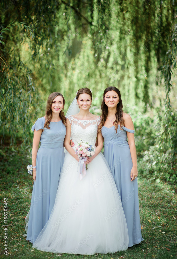 Bridesmaids in blue dresses surround pretty bride on green lawn
