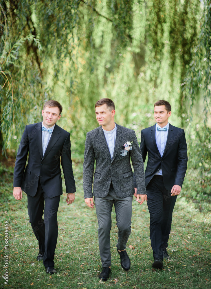 Groom and groomsmen in blue shirts cross green lawn Groom and groomsmen in blue shirts cross green lawn