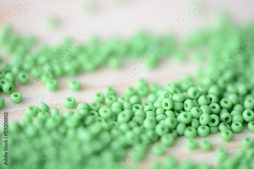 Scattered seed beads of light green color on a wooden background