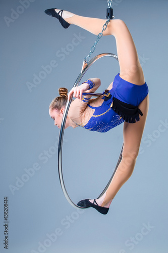 Young woman hanging in aerial ring on a blue background