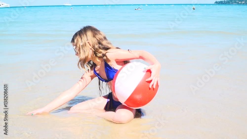 mädchen mit blauem bikini sitzt im meer und spielt mit wasserball