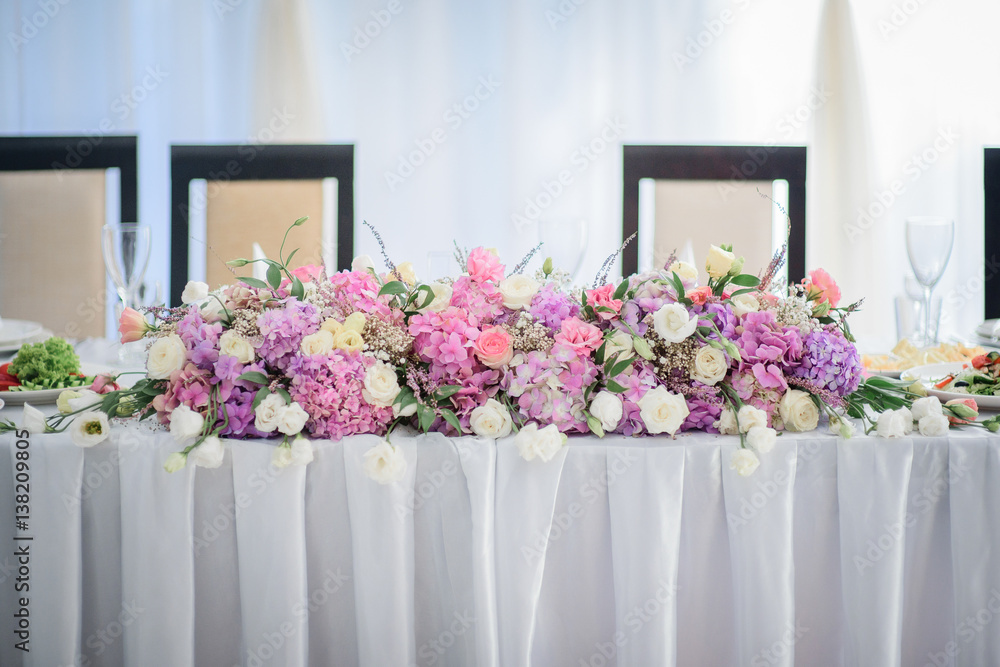 Garland of pink hydrangeas and white roses lies on long dinner table