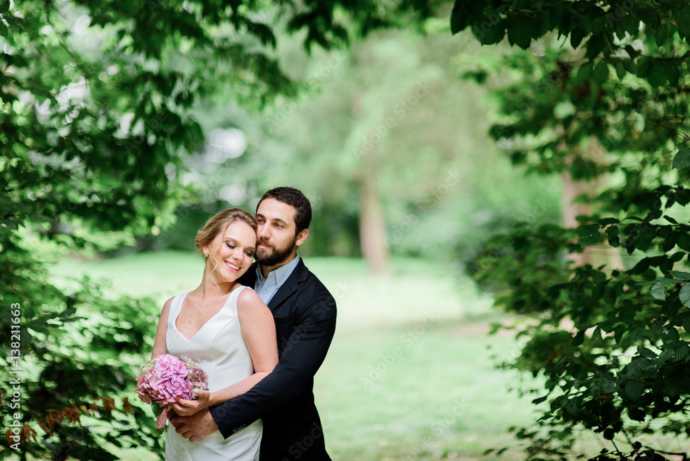 Warm hugs of happy wedding couple standing in the arch of greenery Warm hugs of happy wedding couple standing in the arch of greenery