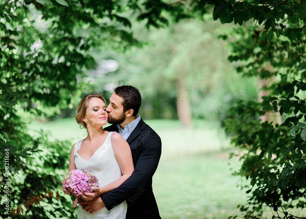 Bearded groom kisses bride while they stand under arch of greenery Bearded groom kisses bride while they stand under arch of greenery