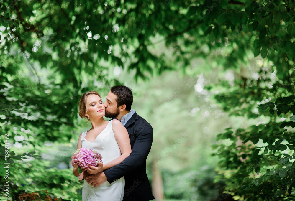 Bearded groom kisses bride while they stand under arch of greenery Bearded groom kisses bride while they stand under arch of greenery