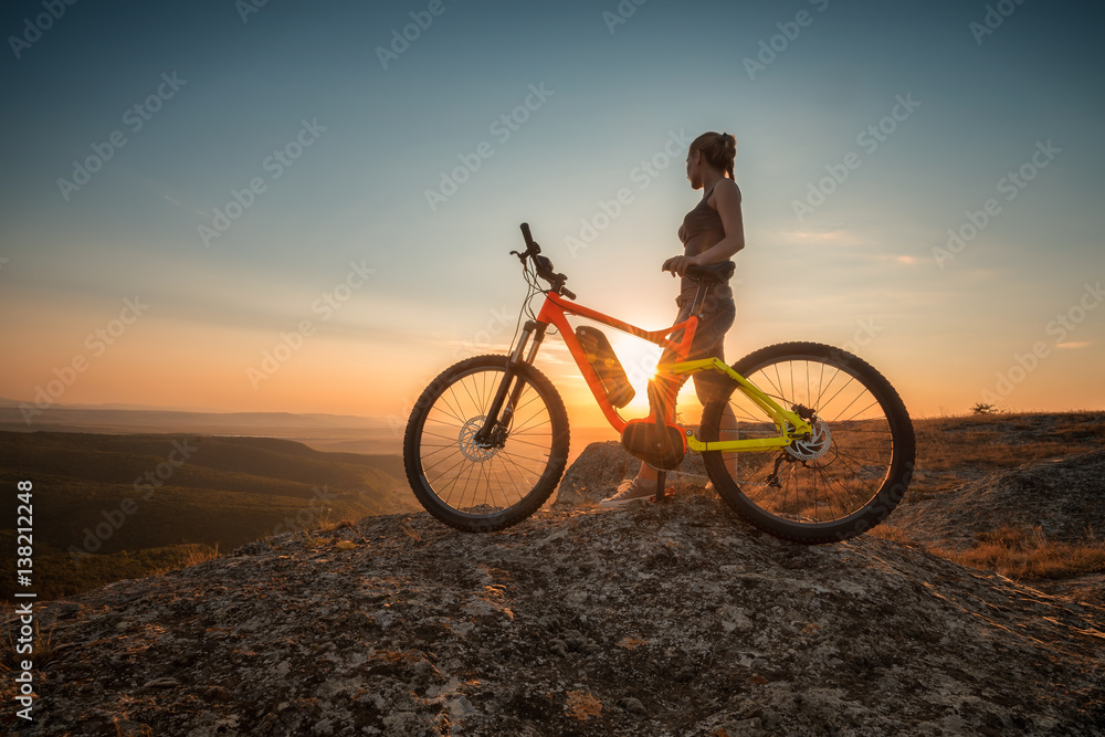 Active life /
A woman with a bike enjoys the view of sunset over an autumn forest