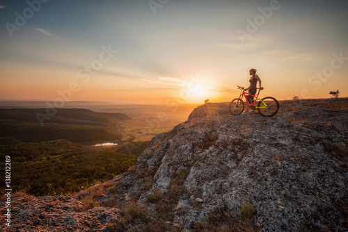 Active life / A woman with a bike enjoys the view of sunset over an autumn forest