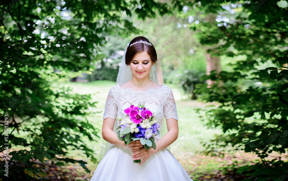 Bride looks on her bouquet while she stands under arch of green branches Bride looks on her bouquet while she stands under arch of green branches