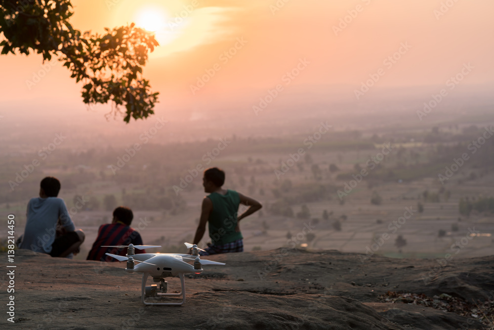 Quad copter put on a rock ground at beautiful twilight sky with silhouette people and tree branch.
drone, Aerial Vehicle with people at sundown and copy space. 