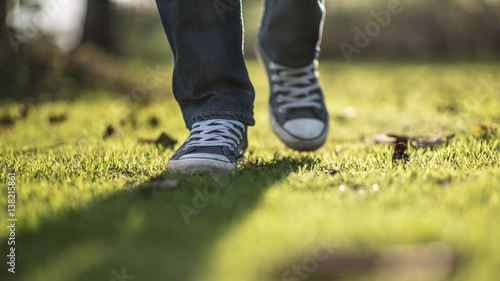 Walking feet ; Man wear blue jean and canvas sneaker sunrise walking on sunrise lawn and landscape background.