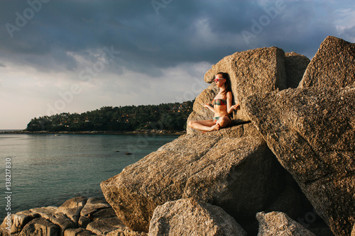 Woman meditating on rock. Woman wearing bikini sitting in lotus position on a rock