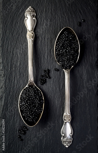 Two vintage silver spoons with black sturgeon caviar on black slate stone background. Top view, flat lay, copy space