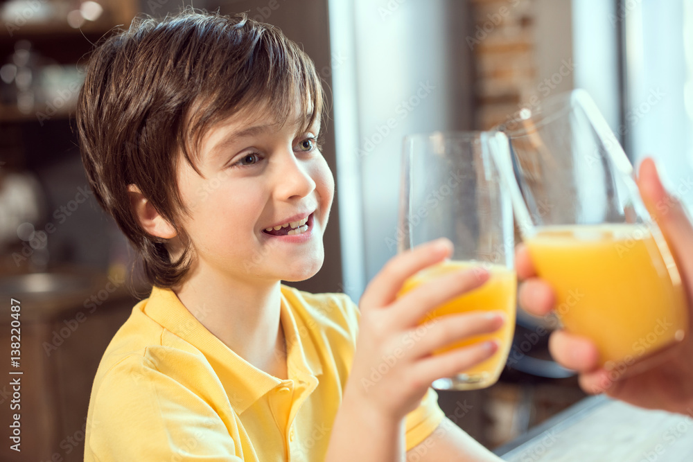 Smiling little boy and father clinking glasses with fresh juice Smiling little boy and father clinking glasses with fresh juice