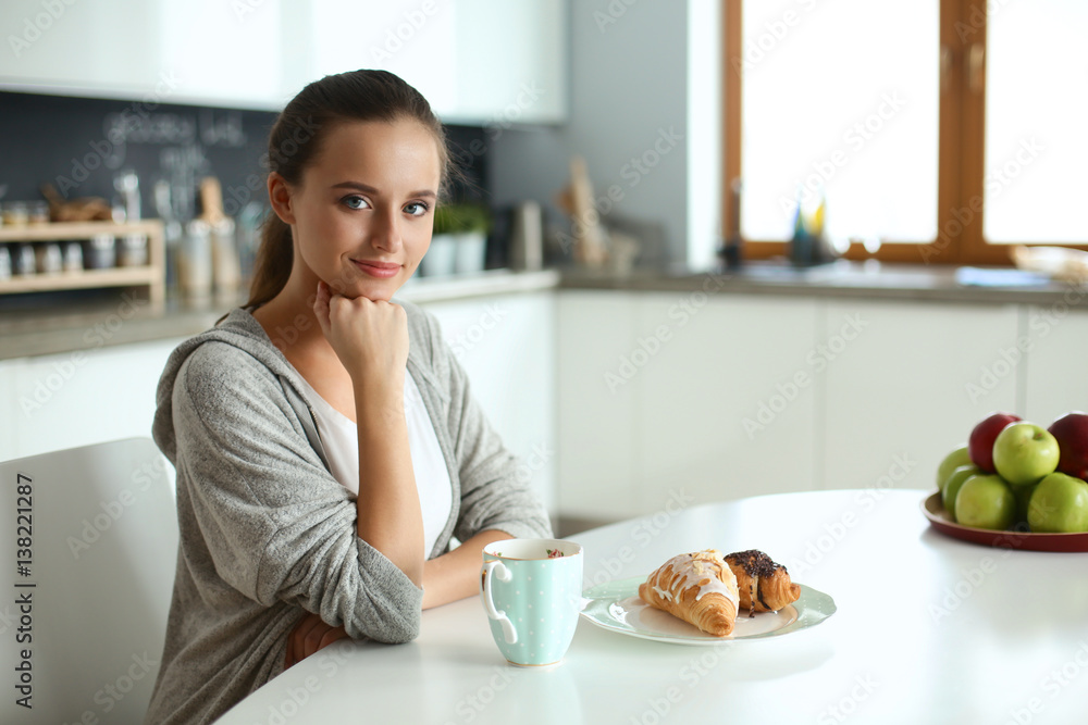 Woman drinking tea with sweet croissant at the kitchen table Woman drinking tea with sweet croissant at the kitchen table