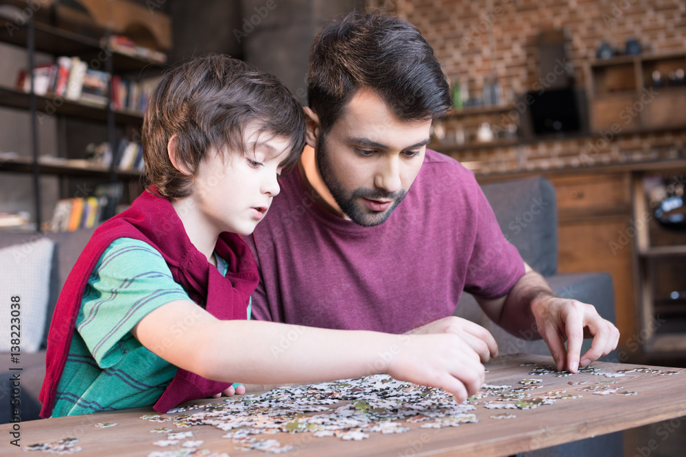 Fototapeta premium side view of focused father and son playing with puzzles at home