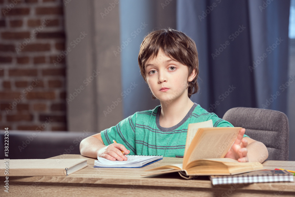 portrait of serious boy sitting at table and doing homework portrait of serious boy sitting at table and doing homework