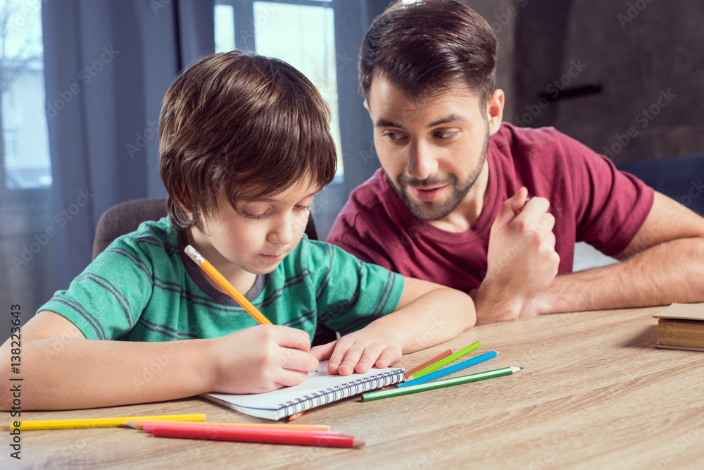 side view of father looking at concentrated son doing homework side view of father looking at concentrated son doing homework