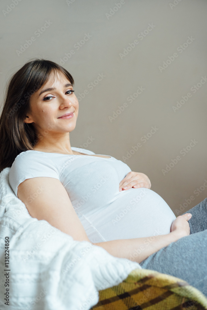 A young pregnant woman with cup sitting in old armchair near the window of a house that is being renovated. A young pregnant woman with cup sitting in old armchair near the window of a house that is being renovated.