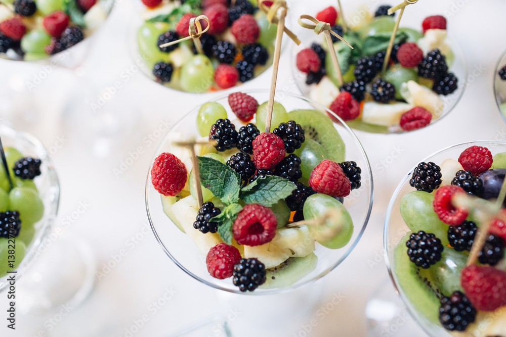 The vase with grapes,raspberries,kiwis and blackberries stand on the buffet table The vase with grapes,raspberries,kiwis and blackberries stand on the buffet table