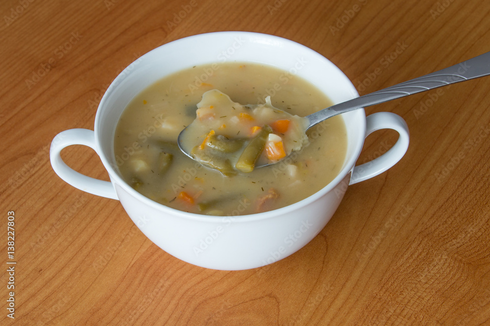 Vegetable soup and silver spoon in a white bowl on wooden background. Vegetable soup and silver spoon in a white bowl on wooden background.