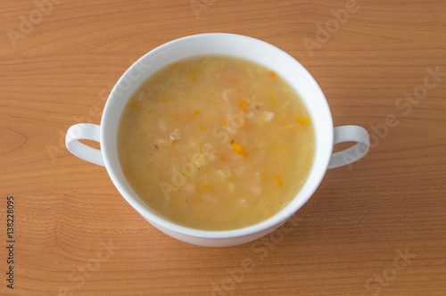 Polish cabbage soup in a white bowl on wooden background. Soup knows in Poland as Kapusniak.