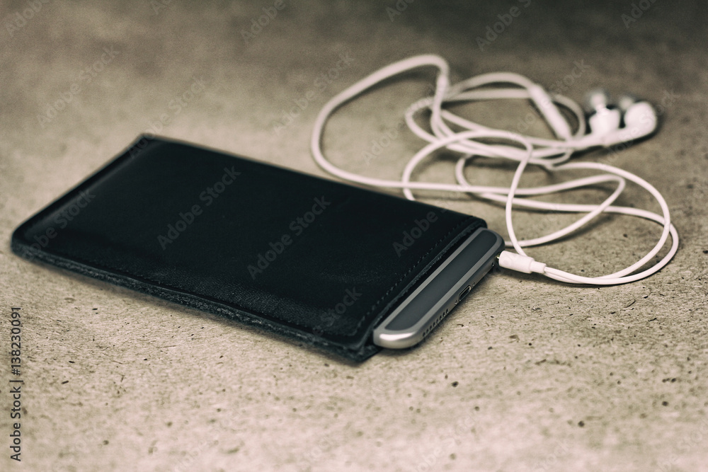 black case for smartphone and white headphones, side view, closeup black case for smartphone and white headphones, side view, closeup