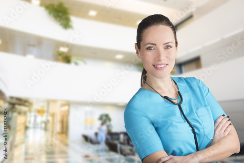 beautiful woman nurse or doctor with crossed arms in front of a blurry hospital lobby background with copy space for advertising Free Download beautiful woman nurse or doctor with crossed arms in front of a blurry hospital lobby background with copy space for advertising - GFXLoad