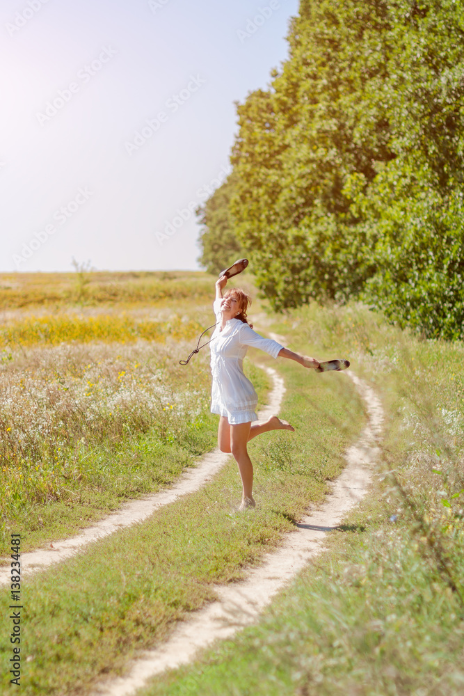 Young beautiful woman running in grass barefoot and holding shoes in hands Young beautiful woman running in grass barefoot and holding shoes in hands