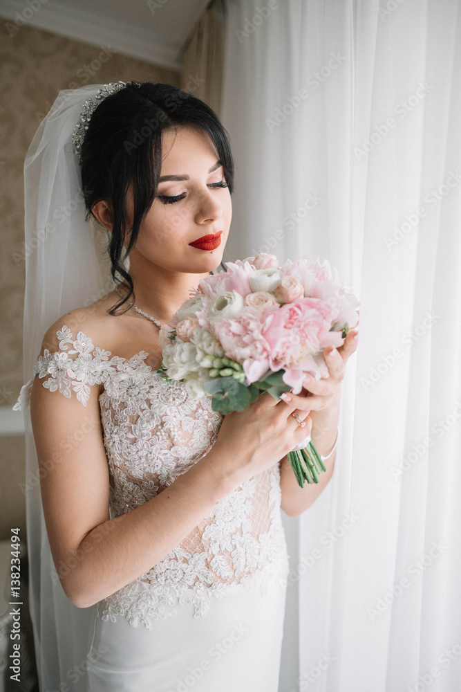 beautiful and young bride with bouquet of flowers standing near window beautiful and young bride with bouquet of flowers standing near window