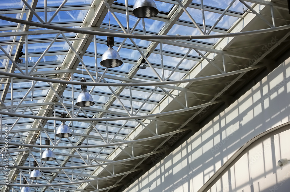 Fragment of modern building with roof made of glass and metal with row of lamps against blue sky background
Fragment of modern building with roof made of glass and metal with row of lamps against blue sky background