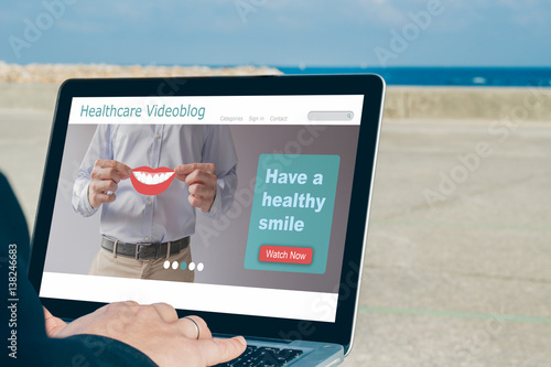 Man using laptop with healthcare videoblog on the screen outdoors in front of the sea.